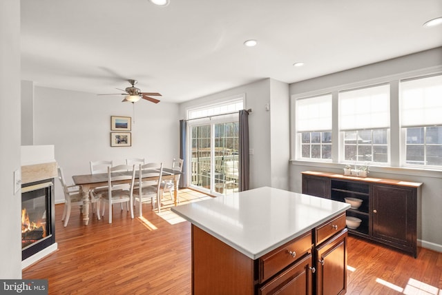 kitchen featuring light wood finished floors, recessed lighting, a multi sided fireplace, ceiling fan, and light countertops