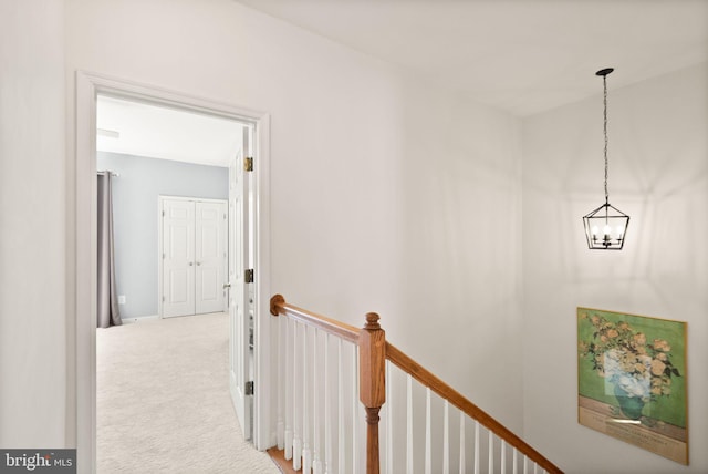 hall with an upstairs landing, carpet, and an inviting chandelier