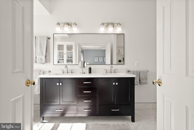 full bath with double vanity, marble finish floor, and a sink