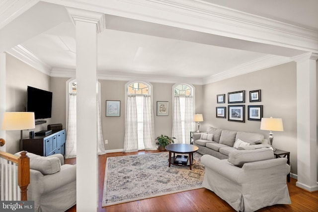 living area with decorative columns, baseboards, wood finished floors, and ornamental molding