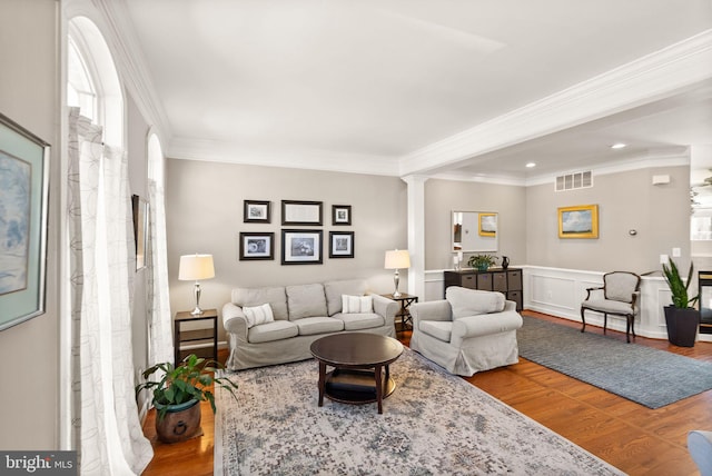 living area with visible vents, ornamental molding, ornate columns, and wood finished floors