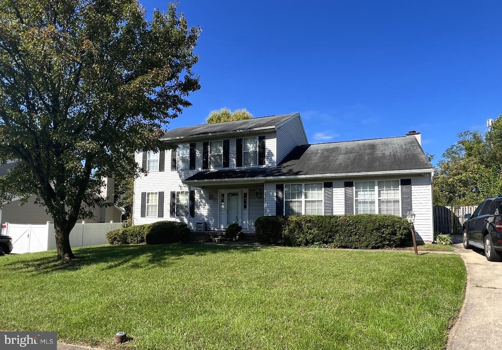 colonial-style house featuring fence and a front lawn