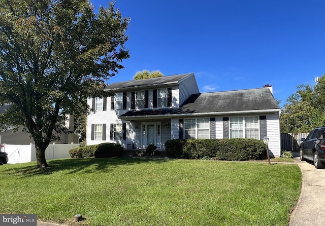 colonial-style house featuring fence and a front lawn