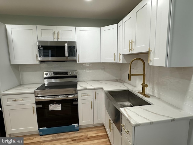 kitchen with light hardwood / wood-style floors, white cabinetry, stainless steel appliances, and light stone counters