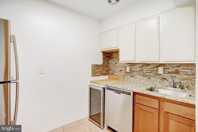 kitchen with stainless steel appliances, beverage cooler, sink, light tile patterned floors, and white cabinetry