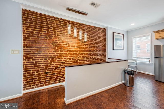 kitchen with dark wood-type flooring, hanging light fixtures, stainless steel refrigerator, crown molding, and brick wall