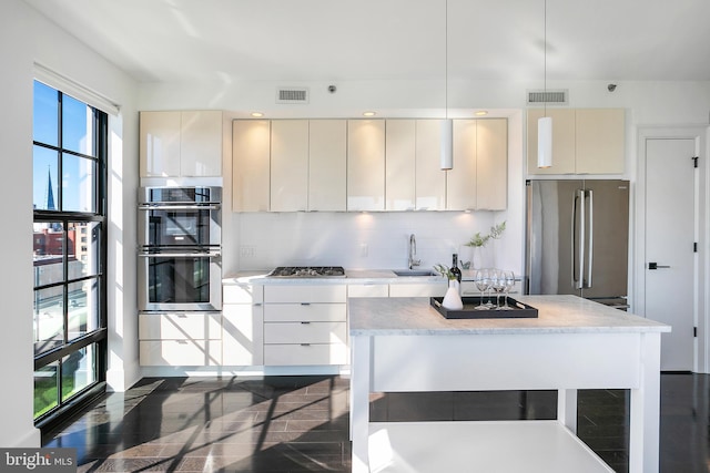 kitchen featuring appliances with stainless steel finishes, backsplash, sink, pendant lighting, and a center island