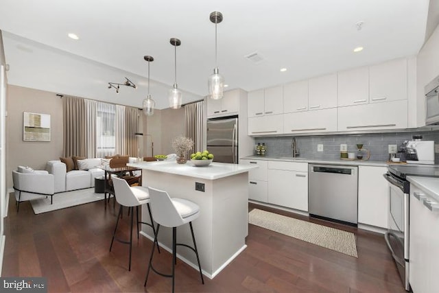 kitchen with pendant lighting, a center island, white cabinets, stainless steel appliances, and dark hardwood / wood-style flooring