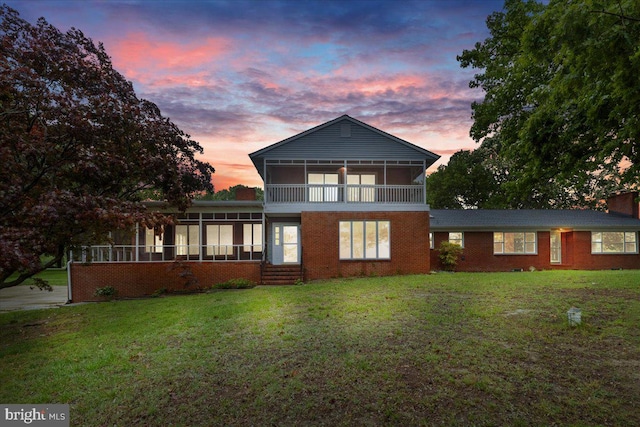 back house at dusk featuring a sunroom and a yard