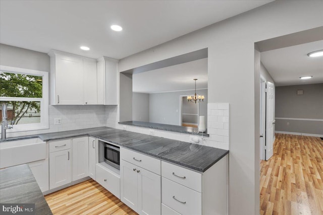 kitchen featuring light hardwood / wood-style flooring, backsplash, white cabinetry, a notable chandelier, and stainless steel microwave