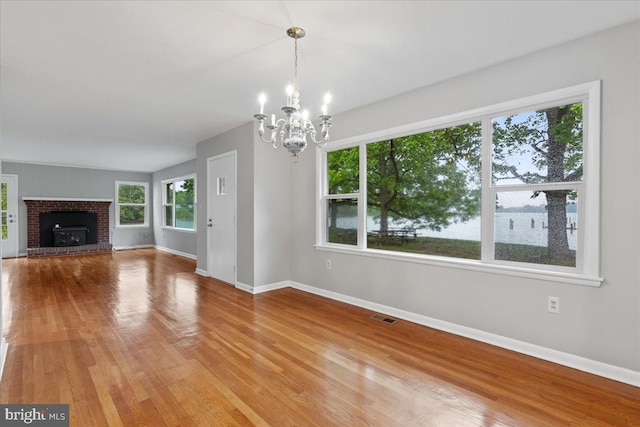 unfurnished living room with wood-type flooring, a fireplace, and a chandelier