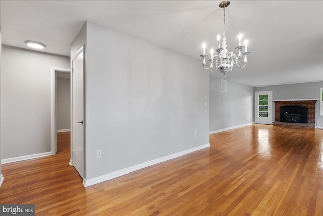 unfurnished living room with a notable chandelier, a brick fireplace, and hardwood / wood-style floors