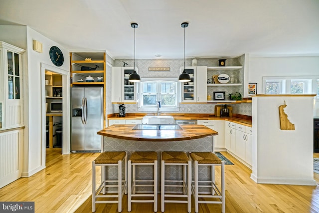 kitchen with stainless steel fridge with ice dispenser, white cabinetry, butcher block counters, light hardwood / wood-style floors, and decorative light fixtures