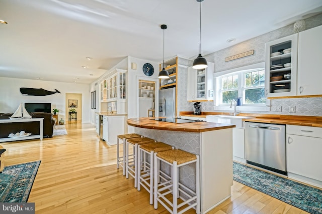 kitchen featuring appliances with stainless steel finishes, light wood-type flooring, butcher block countertops, decorative light fixtures, and white cabinets