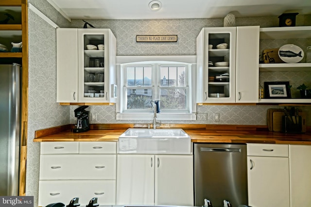 kitchen with white cabinetry, butcher block counters, stainless steel appliances, and sink