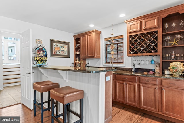 bar with light hardwood / wood-style flooring and dark stone counters