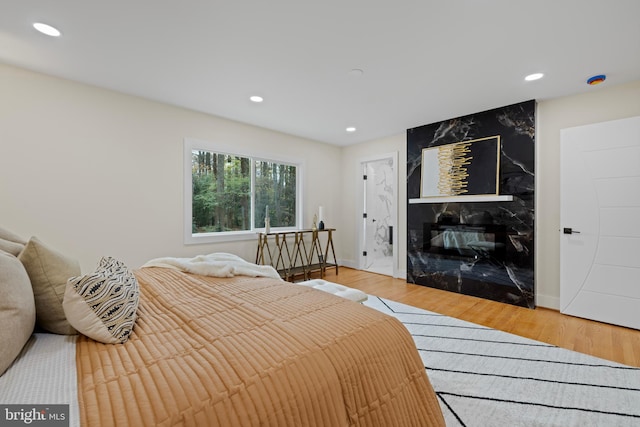 bedroom featuring light wood finished floors, a premium fireplace, baseboards, and recessed lighting