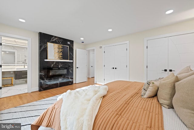 bedroom featuring recessed lighting, wood finished floors, a fireplace, and two closets