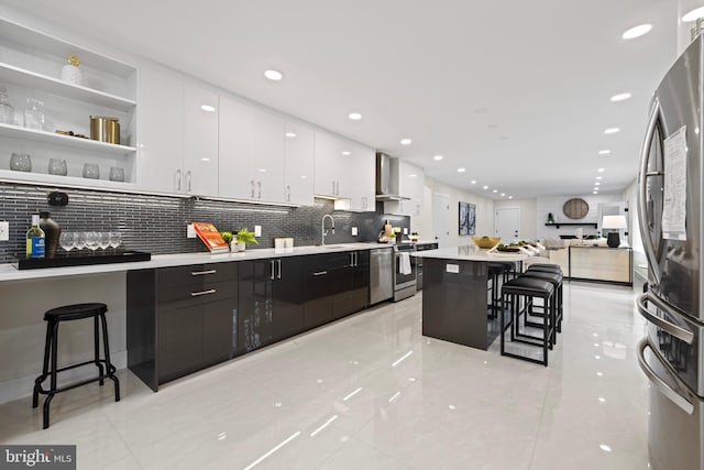 kitchen featuring stainless steel appliances, white cabinetry, a kitchen breakfast bar, wall chimney range hood, and modern cabinets