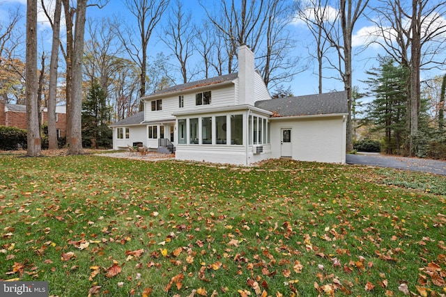 back of house with a sunroom, a lawn, and a chimney