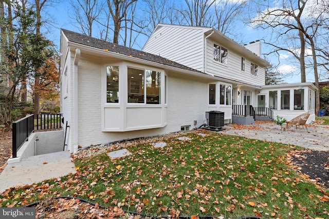 exterior space featuring a sunroom, a chimney, cooling unit, a yard, and brick siding