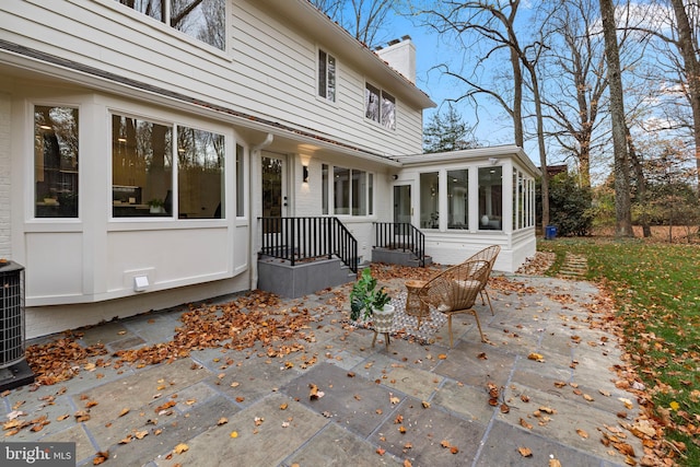 back of house with a sunroom, a patio area, brick siding, and a chimney