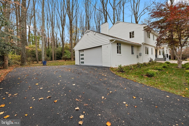 view of side of property with a garage, brick siding, driveway, and a chimney