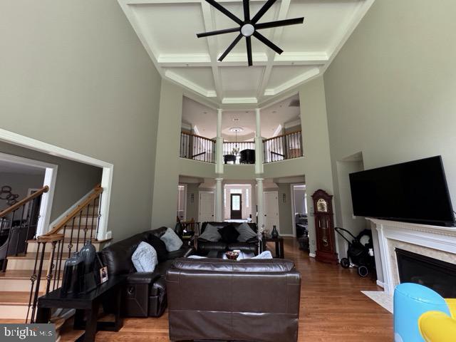 living room featuring ceiling fan, hardwood / wood-style flooring, a premium fireplace, coffered ceiling, and decorative columns