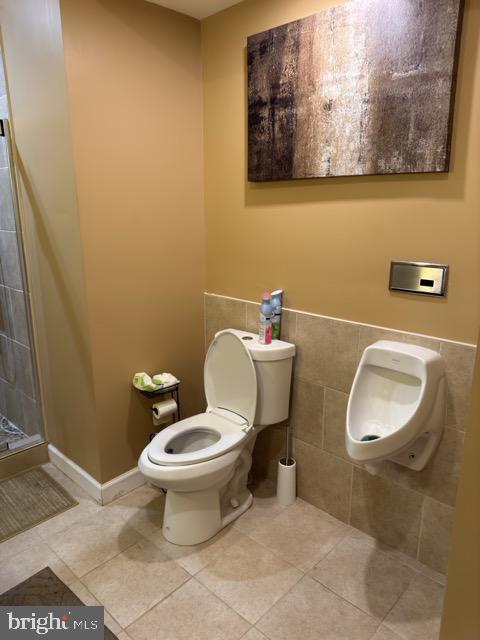 bathroom featuring tile patterned flooring, tile walls, toilet, and a shower