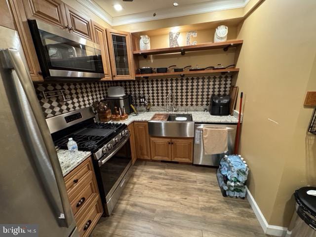 kitchen with light stone counters, ornamental molding, light hardwood / wood-style flooring, appliances with stainless steel finishes, and backsplash