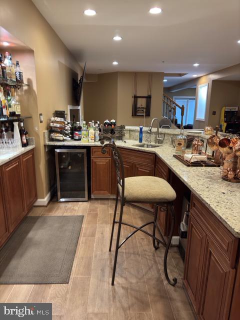 kitchen with light stone counters, wine cooler, sink, kitchen peninsula, and light hardwood / wood-style floors