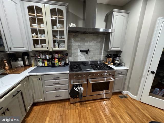 kitchen with gray cabinetry, light hardwood / wood-style floors, wall chimney range hood, and double oven range