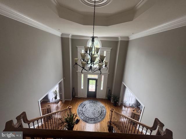 entryway with a tray ceiling, hardwood / wood-style floors, ornamental molding, and a chandelier