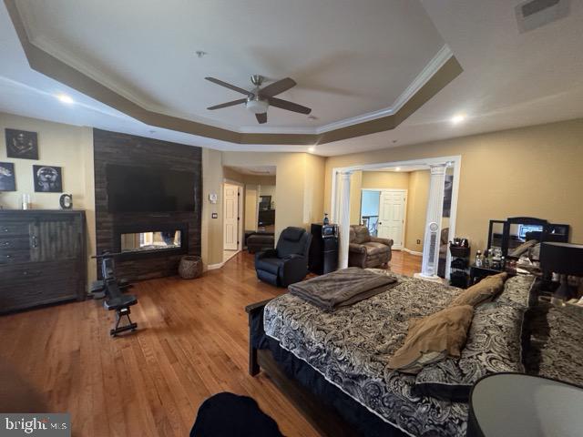 bedroom with ceiling fan, a raised ceiling, ornamental molding, a fireplace, and hardwood / wood-style floors