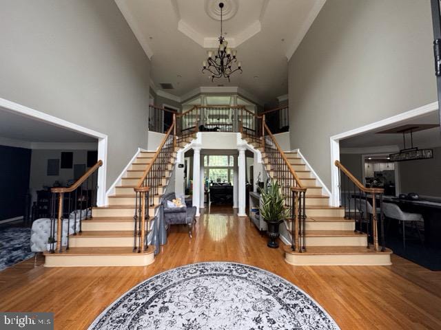 foyer entrance featuring wood-type flooring, a high ceiling, ornate columns, a chandelier, and ornamental molding