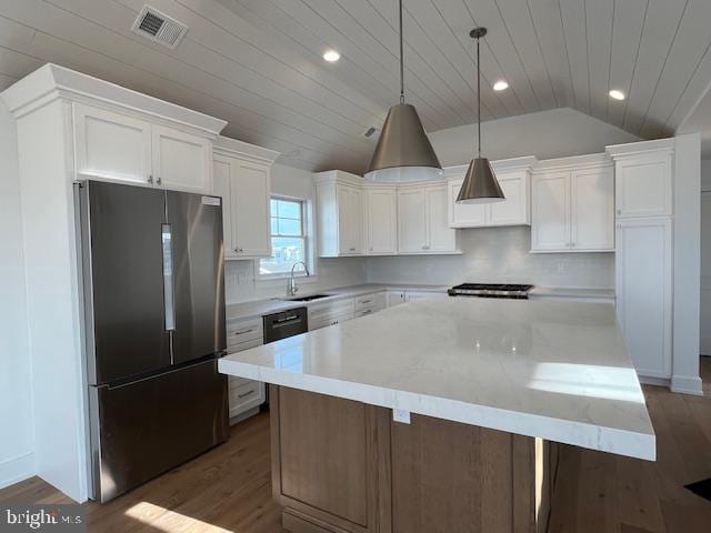 kitchen with stainless steel fridge, a kitchen island, white cabinetry, hanging light fixtures, and lofted ceiling