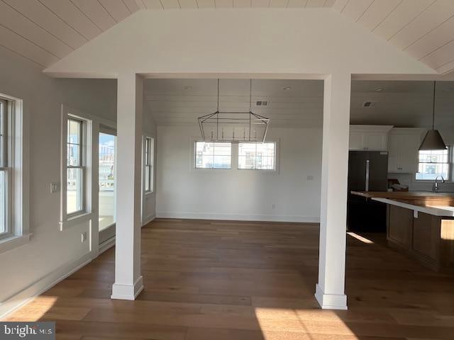 unfurnished dining area with an inviting chandelier, dark hardwood / wood-style flooring, sink, and vaulted ceiling