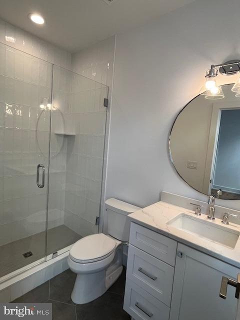 bathroom featuring tile patterned flooring, vanity, toilet, and a shower with door