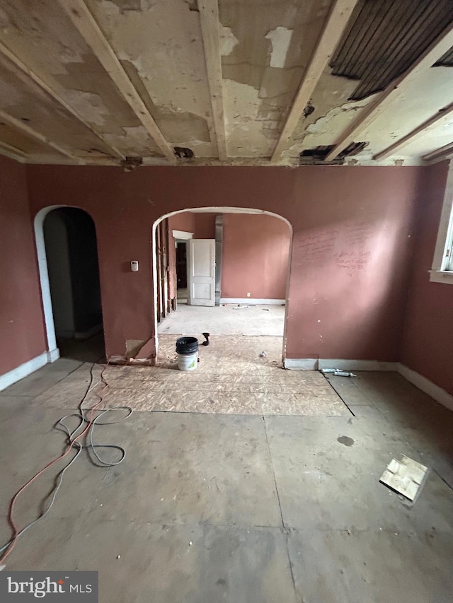 empty room featuring arched walkways and baseboards