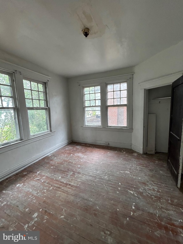 unfurnished bedroom featuring multiple windows, hardwood / wood-style floors, and baseboards