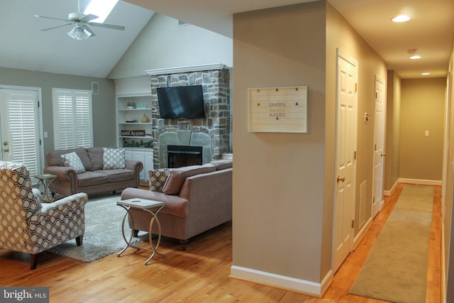 living room featuring light hardwood / wood-style floors, a fireplace, high vaulted ceiling, a skylight, and ceiling fan