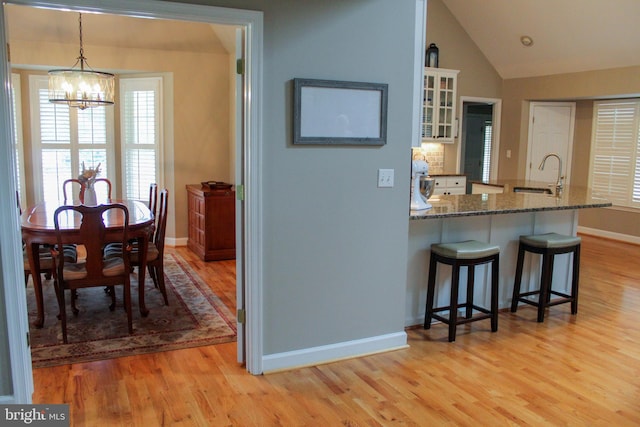 kitchen with a kitchen breakfast bar, white cabinets, pendant lighting, light wood-type flooring, and lofted ceiling