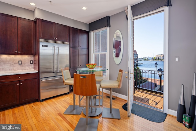 kitchen with a water view, backsplash, built in fridge, and light wood-type flooring