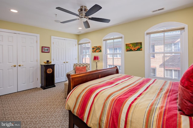 bedroom featuring multiple closets, light colored carpet, and ceiling fan