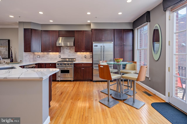 kitchen featuring wall chimney exhaust hood, high quality appliances, light hardwood / wood-style flooring, kitchen peninsula, and ornamental molding