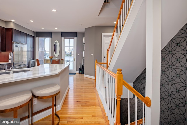 kitchen with light stone countertops, sink, light wood-type flooring, kitchen peninsula, and a breakfast bar