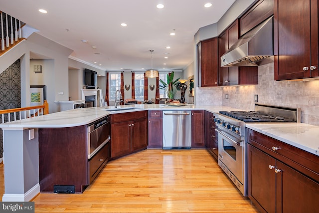 kitchen featuring wall chimney exhaust hood, light hardwood / wood-style flooring, kitchen peninsula, pendant lighting, and appliances with stainless steel finishes