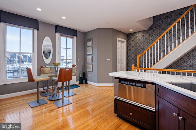 kitchen with dark brown cabinetry, a healthy amount of sunlight, light stone countertops, and light wood-type flooring