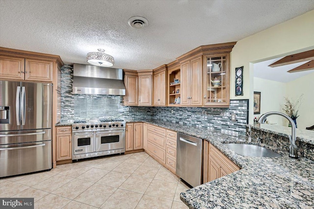 kitchen featuring decorative backsplash, dark stone countertops, stainless steel appliances, sink, and wall chimney range hood