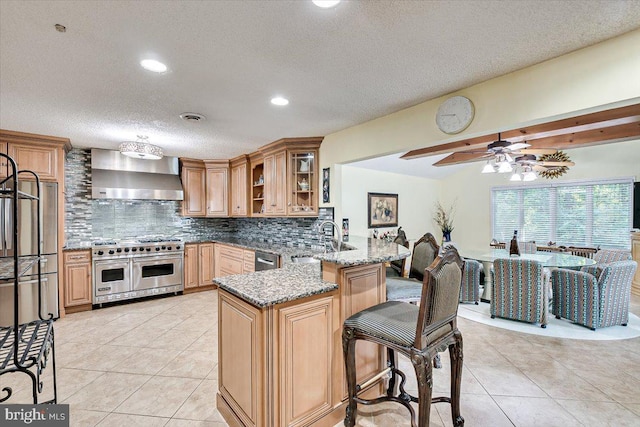 kitchen featuring appliances with stainless steel finishes, light stone counters, kitchen peninsula, sink, and wall chimney range hood